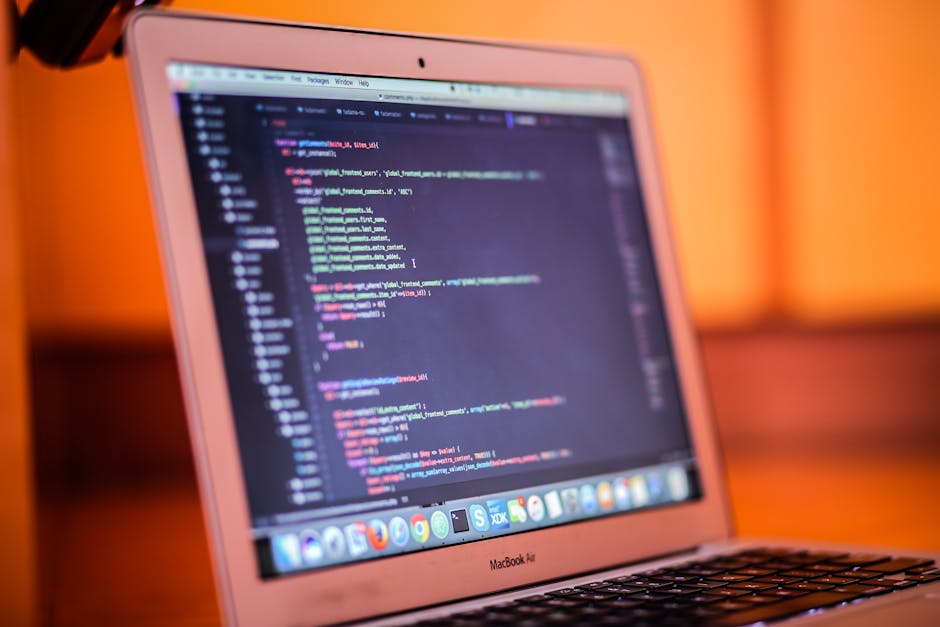 A close-up view of a MacBook Air laptop displaying lines of code on its screen, set against a warm, orange-hued background. The keyboard is visible at the bottom, and the screen shows a dark-themed co